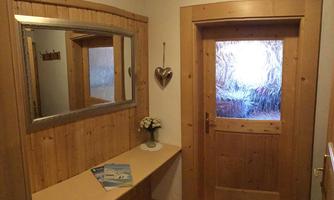 An inviting entrance area with wooden paneling and a large mirror. The glass door lets in light and showcases a warm atmosphere.