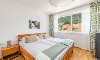 A bright bedroom with a double bed and wooden wardrobes. Large windows offer a view of the landscape and let in plenty of light.