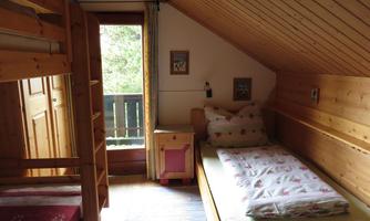 A cozy bedroom with wood paneling and a bunk bed. Large window with an outside view and simple furnishings.
