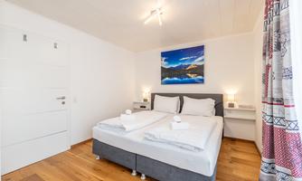A modern bedroom with a double bed and soft bedding. A picture of a landscape hangs on the wall, and there is soft lighting on the nightstands.