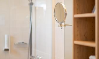 A modern bathroom with a glass shower and an elegant sink. On the wall, there is a mirror and a wooden shelf with towels.