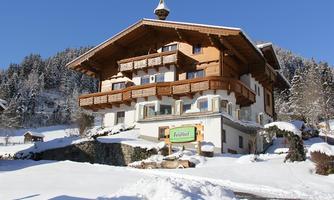 A cozy chalet in the snow with wooden balustrades. The sky is clear and the surroundings are surrounded by snow-covered trees.