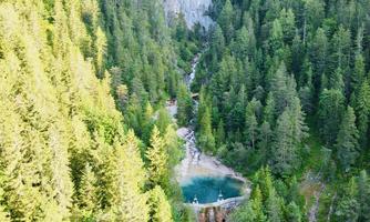 A picturesque landscape with dense, green forests and a clear blue lake. In the background, a waterfall flows through nature.