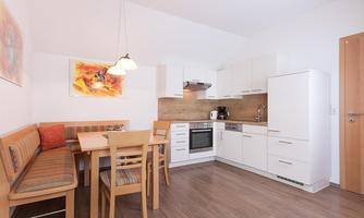 A modern kitchen with bright furniture and a dining area. Colorful pictures hang on the wall.