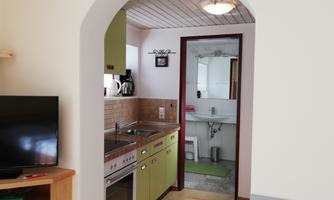 A small apartment with a modern kitchen and a bathroom in the background. The room is brightly and invitingly furnished.
