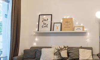 A cozy living space with a gray couch and a wooden table. Pictures are hanging on the wall and there is soft lighting.