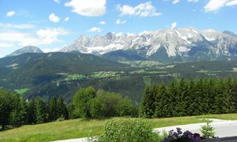An impressive mountain landscape with snow-capped peaks and green valleys. The sky is blue with a few white clouds.
