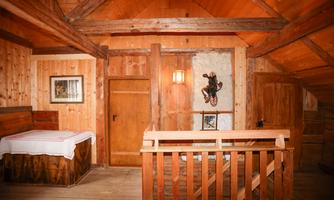A cozy wooden cabin with warm wood tones and rustic charm. Inside, there are a bed, a staircase, and decorative elements visible.
