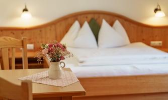 A cozy bedroom with a large bed and white pillows. On the table, there is a small vase with colorful flowers.