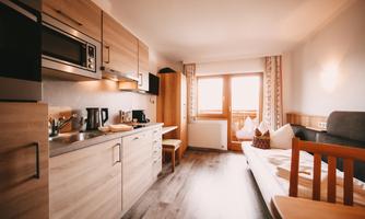 A modern kitchen unit with wooden cladding in a cozy room. The living room has a view of the window with daylight.