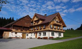 A traditional wooden house with balconies in a picturesque landscape. The sky is clear and the surroundings are green and inviting.