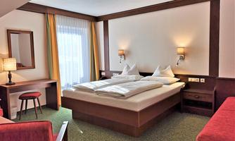 A cozy hotel room with a double bed and two nightstands. There is a desk and a chair, as well as large windows with curtains.