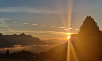 A beautiful sunset over mountains with stunning colors. The light shines through the trees and the sky is clear and blue.