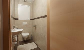 A modern bathroom with bright tiles and a sink. On the right is a toilet and a small rug on the floor.