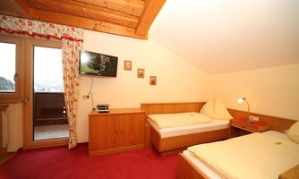 A cozy bedroom with two single beds and wooden decor. The room has a television and balcony access.