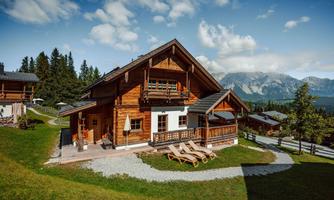A beautiful wooden house in the mountains with a green meadow. In the background, mountains and a blue sky are visible.