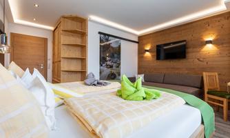 A cozy room with a double bed and modern furniture. The walls are in warm wood tones and there is a sitting area.