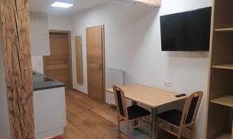 A modern living area with a table and chairs as well as a small kitchenette. The walls are light, and there are wood-paneled details.