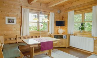 A cozy wooden room with a table, a bench, and a television. Bright windows bring in plenty of daylight and create an inviting atmosphere.