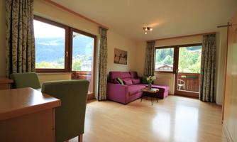 A modern living room with a purple sofa and a table. Large windows provide a beautiful view of the landscape.