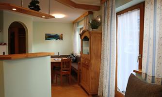 A cozy living area with a dining table and a wooden dresser. Large windows let in plenty of natural light.
