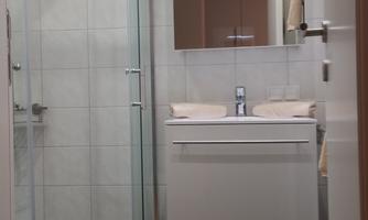 A modern bathroom with a glass shower and a white sink. The walls are light tiled and the floor is dark brown.