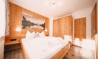 A cozy bedroom with wooden paneling and a large bed. A landscape painting hangs on the wall, creating a calm atmosphere.