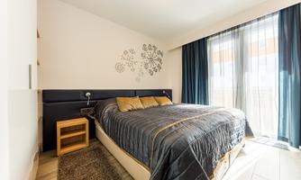 A modern bedroom with a large bed and elegant bedding. Large windows allow plenty of daylight in and create a friendly atmosphere in the room.