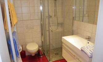 A modern bathroom with a glass shower enclosure and a white sink. The colors are bright and friendly, with towels in soft tones.
