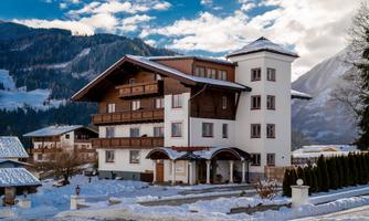 A charming hotel in the mountains, surrounded by snow-covered landscapes. The sky is clear with some clouds.