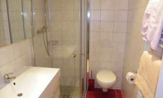 A modern bathroom with a shower, sink, and toilet. The walls are tiled, and the fixtures are simple and functional.