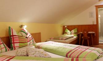 A cozy bedroom with two beds and colorful blankets. In the background, there is a small table and a bathroom.