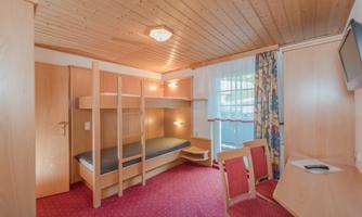 A simple room with a wooden ceiling and two bunk beds. The room is bright and friendly, with a table and two chairs.