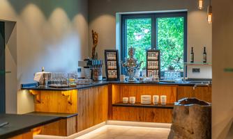 A modern-designed interior with a wooden bar and a window overlooking greenery. Glasses and drinks are ready on the counter.