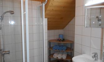 A modern bathroom with a shower and a sink. Shelves with towels and decorative elements complement the space.