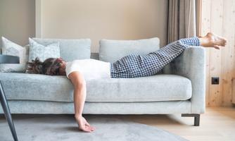 A person is lying relaxed on a gray sofa. They are wearing a white blouse and checkered pants.