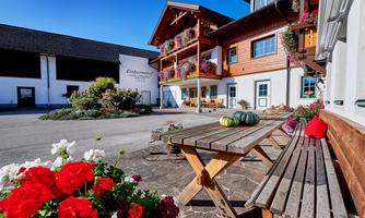 An inviting wooden building with colorful flower boxes. In the courtyard, there are wooden tables and benches surrounded by blooming plants.