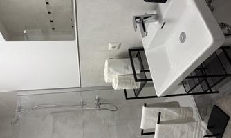 A modern bathroom with a shower and a white sink. Towels and toilet paper are neatly arranged.
