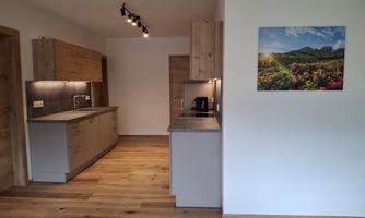 A modern kitchen with wooden shelves and a bright, open space. A colorful landscape graphic hangs on the wall.