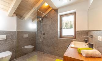 A modern bathroom with a large glass shower and wooden ceiling. Bright tiles and an elegant sink complement the stylish atmosphere.