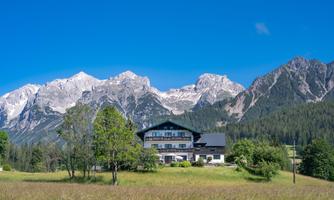 A picturesque alpine building surrounded by green meadows and tall mountains. The radiant blue sky gives the scene a peaceful atmosphere.
