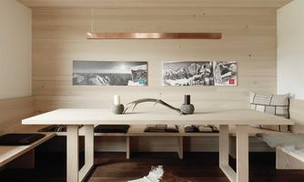A modern living room with wood paneling and a minimalist decor. The room features a large table, decorated with candles and pictures of mountains.