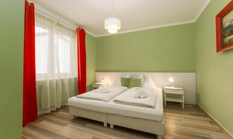 A modern bedroom with green walls and red curtains. The room is bright and cozy with a double bed and nightstands.