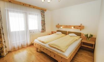 A bright bedroom with two single beds and wooden furniture.  
Large windows provide plenty of daylight and a cozy atmosphere.