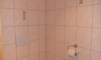 A simple bathroom with white tiles and a toilet. There is a holder for toilet paper on the wall.