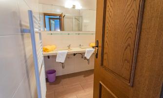 A clean bathroom with two sinks and large mirrors. Towels are neatly arranged, and the door is open.