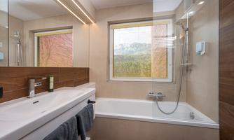 A modern bathroom with a bathtub and shower. The window lets in plenty of daylight and creates a bright atmosphere.