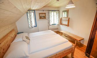 A cozy bedroom with a double bed and wooden decor. The windows let in plenty of daylight and the room is simply furnished.