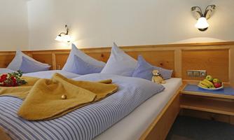 A cozy bedroom with two beds and blue cushions. On the nightstand are fresh fruits and a small figure.
