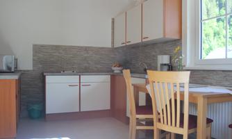 A bright kitchen with modern furniture and a small dining table. The walls are designed with light tiles and a window lets in plenty of daylight.